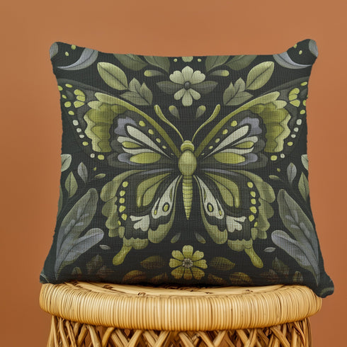 A square decorative pillow featuring an intricately detailed butterfly design in olive green, sage, and cream colors against a black background. The butterfly is surrounded by botanical elements with symmetrical floral patterns.